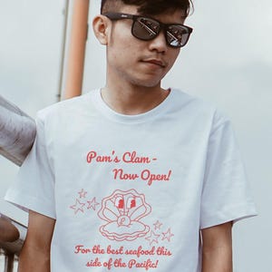 Pam's Clam Tee, Unisex T-Shirt mit Slogan Cartoon Charakter, lustiges Grafikshirt, humorvolles Top, Geschenk für Fischliebhaber, Neuheit-T-Shirt
