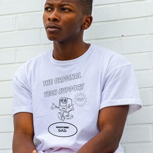 May include: White t-shirt with the text "THE ORIGINAL TECH SUPPORT" and a cartoon computer graphic. Below the graphic is the text "ALWAYS THERE! DAD". The person is wearing red shorts.