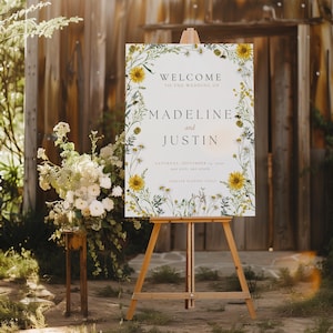 Op de afbeelding: Een wit welkomsbord voor een bruiloft met een bloemrijke rand met zonnebloemen en andere wilde bloemen. Het bord staat er: "Welkom op de bruiloft van Madeline en Justin, zaterdag 14 september 2020, Any City, Any State, Forever Happens Today".