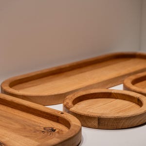 Könnte beinhalten: Eine Sammlung von Holztabletts in verschiedenen Formen und Größen. Die Tabletts sind aus hellbraunem Holz gefertigt und haben eine glatte Oberfläche. Die Formen umfassen ein Oval, ein langes Oval und ein rundes Tablett. Die Tabletts werden auf einer weißen Oberfläche präsentiert.