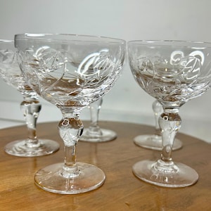 Peut inclure: Ensemble de cinq coupes à champagne en verre transparent à pied avec un motif en verre taillé. Les verres sont disposés sur une surface en bois.