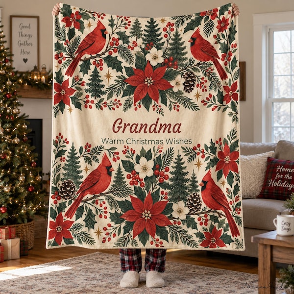 Op de afbeelding: Een crèmekleurige plaid met een herhalend patroon van rode kardinalen, groene dennenbomen, rode kerststerren en dennenappels. De tekst in het midden luidt "Grandma" in een schrijfletter boven "Warm Christmas Wishes".