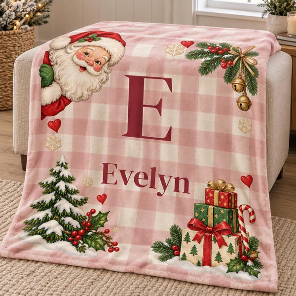 Op de afbeelding: Een zachte roze en witte geruite deken met een vintage kerstmanillustratie, een grote letter E, de naam Evelyn, een kerstboom en een stapel ingepakte cadeaus versierd met hulst en gouden kerstbelletjes.