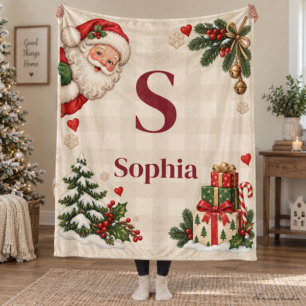 Op de afbeelding: Een crèmekleurige plaid met een lichtbeige ruitpatroon, voorzien van een grote bordeauxrode letter S en de naam Sophia. Het ontwerp bevat een vintage kerstman, een besneeuwde dennenboom, rode bessen en gestapelde cadeautjes.