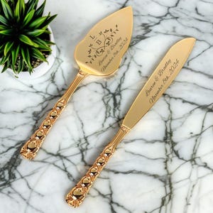 以下が含まれることがあります： 名前と日付が刻まれた金色のウェディングケーキナイフとサーバーのセット。サーバーには「LIB Lauren & Bradley November 8th, 2024」と刻まれています。ナイフには「Lauren & Bradley November 8th, 2024」と刻まれています。