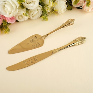 以下が含まれることがあります： 金色のウェディングケーキサーバーとナイフのセット。サーバーは幅広の三角形の刃、ナイフは丸みを帯びた刃です。どちらにも名前と日付が刻印されています。ハンドルには花の模様があります。