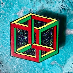 May include: A hexagonal enamel pin featuring an impossible cube design with red, green, and yellow outlines. The interior sections of the cube are filled with a dark, glittery material that reflects light with small, multicolored sparkles.
