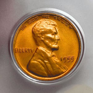 Puede incluir: Una moneda de un centavo Lincoln de 1955 con un retrato de perfil de Abraham Lincoln mirando hacia la derecha. La moneda de color cobre muestra el texto IN GOD WE TRUST en el borde superior, LIBERTY a la izquierda y el año 1955 a la derecha.