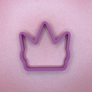 May include: A purple plastic crown cookie cutter. The crown has a pointed top and a rounded bottom.