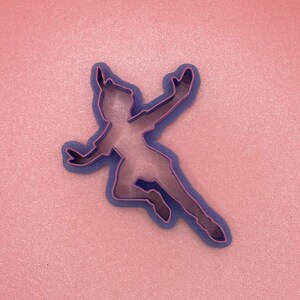 May include: Purple plastic cookie cutter shaped like a person flying with arms outstretched.