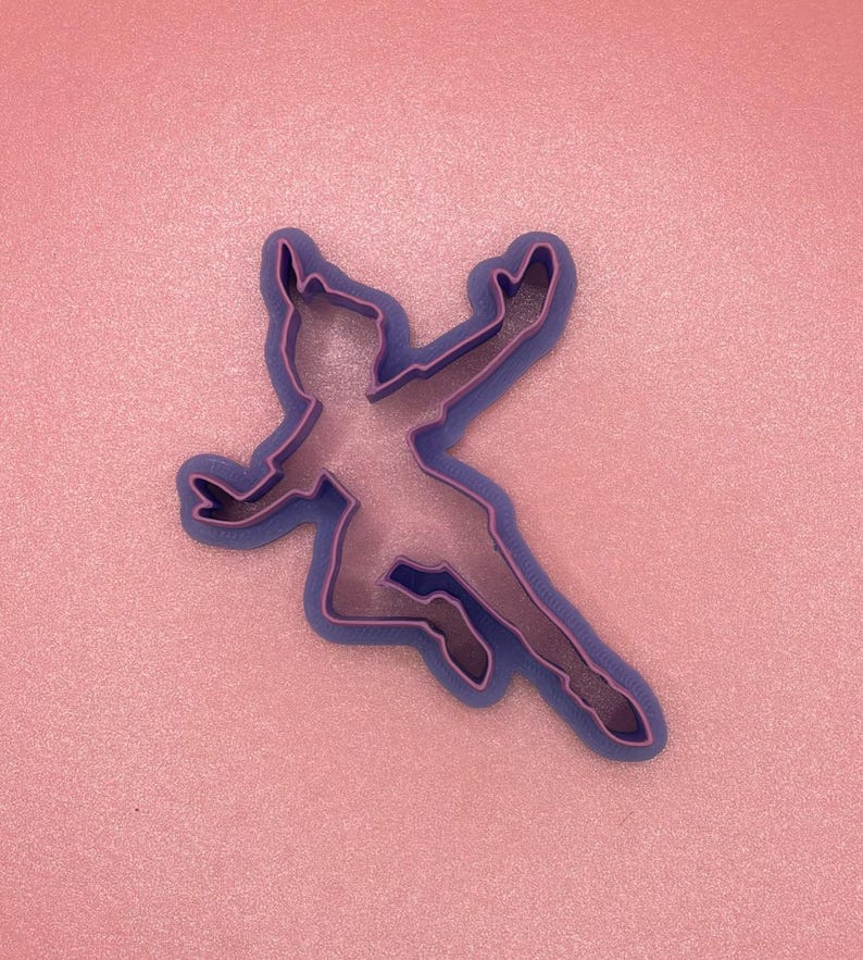 May include: Purple plastic cookie cutter shaped like a person flying with arms outstretched.