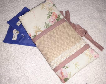 May include: A floral print tea cozy with a woven center panel, lace trim, and pink accents. Two blue tea packets are visible. The cozy has a matching pink ribbon tie.