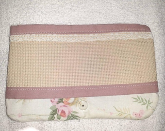 May include: A rectangular, handmade pouch with a beige cross-stitch center, bordered by a pink fabric. A white lace trim separates the cross-stitch from the pink fabric. The bottom features a floral print with pink roses and green leaves.