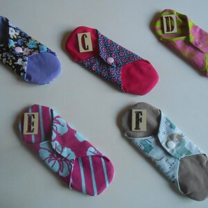 May include: Six cloth menstrual pads with different patterns and colors. Each pad has a letter label, from A to F, sewn on the front.