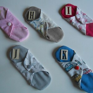 May include: Five reusable cloth pads with different patterns and colors. Each pad has a letter label: G, H, I, J, and K. The pads are folded and ready to use.