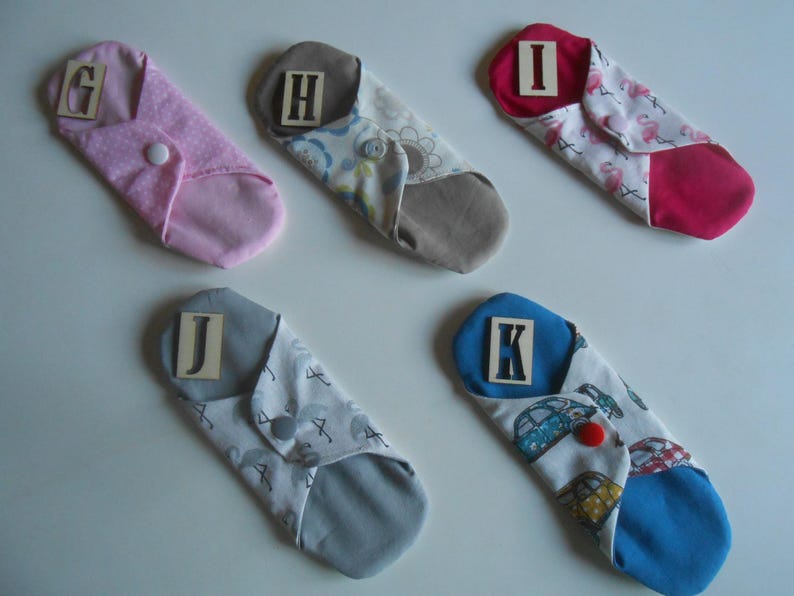 May include: Five reusable cloth pads with different patterns and colors. Each pad has a letter label: G, H, I, J, and K. The pads are folded and ready to use.