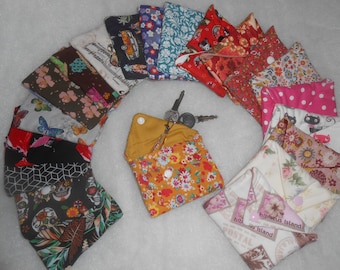 May include: A collection of fabric pouches with various patterns and designs. The pouches are made of different fabrics, including floral, polka dot, and geometric patterns. Some pouches have a zipper closure, while others have a button closure. The pouches are arranged in a circle around a set of keys.