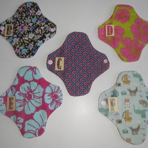 May include: Five reusable cloth pads with different patterns. The pads are labeled with letters A through E. The pads are made of cotton fabric and have a soft, absorbent texture.