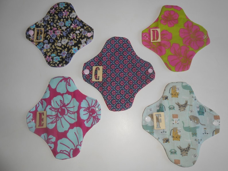 May include: Five reusable cloth pads with different patterns. The pads are labeled with letters A through E. The pads are made of cotton fabric and have a soft, absorbent texture.