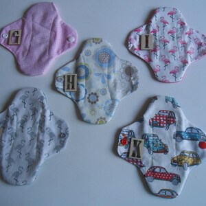 May include: Five different cloth pads with various patterns, including flamingos, cars, and flowers. Each pad has a letter printed on it, from G to K.