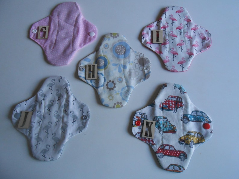 May include: Five different cloth pads with various patterns, including flamingos, cars, and flowers. Each pad has a letter printed on it, from G to K.