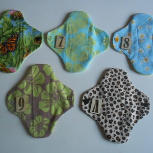 May include: Five reusable cloth menstrual pads with different patterns and numbers 6 through 10 printed on them.