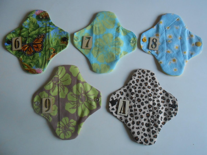 May include: Five reusable cloth menstrual pads with different patterns and numbers 6 through 10 printed on them.