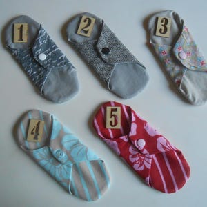 May include: Five reusable cloth menstrual pads in various colors and patterns with numbers 1 through 5 printed on them.