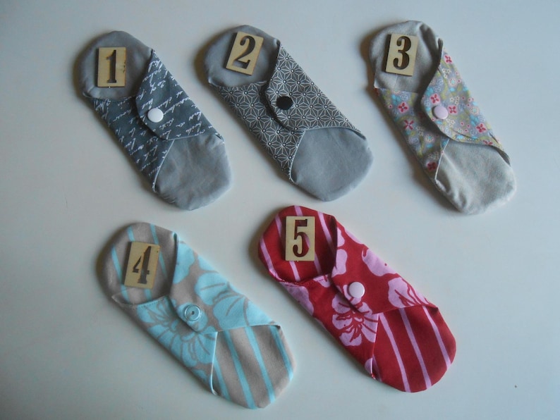 May include: Five reusable cloth menstrual pads in various colors and patterns with numbers 1 through 5 printed on them.