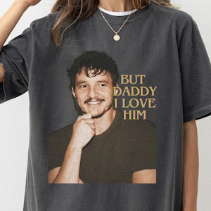 May include: A gray t-shirt with a graphic of a man with a mustache and the text "BUT DADDY I LOVE HIM" printed on the front.