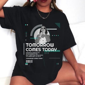 May include: Black t-shirt with the text "TOMORROW COMES TODAY" in white and teal. The shirt features a graphic of a person and geometric shapes. Additional text includes song lyrics. A casual, everyday wear tee.