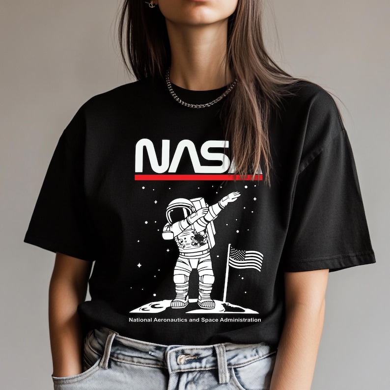 May include: Black t-shirt with a white NASA logo and a white illustration of an astronaut doing the dab on the moon. The text "National Aeronautics and Space Administration" is printed below the image.