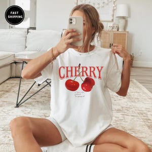 May include: White t-shirt with a red cherry graphic and the text "CHERRY" in red. The text below the cherries reads "If I have a nice soundtrack I'm going out."