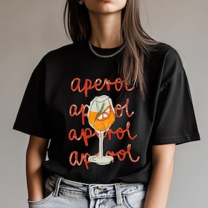May include: Black t-shirt with a red graphic of an Aperol Spritz cocktail. The text "aperol" is repeated four times in a distressed font.
