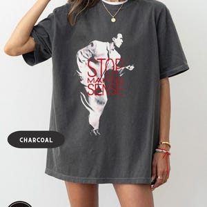 May include: Charcoal-colored t-shirt featuring a graphic of a man in a white suit with the text "STOP MAKING SENSE" in red. The shirt has a vintage, washed look.
