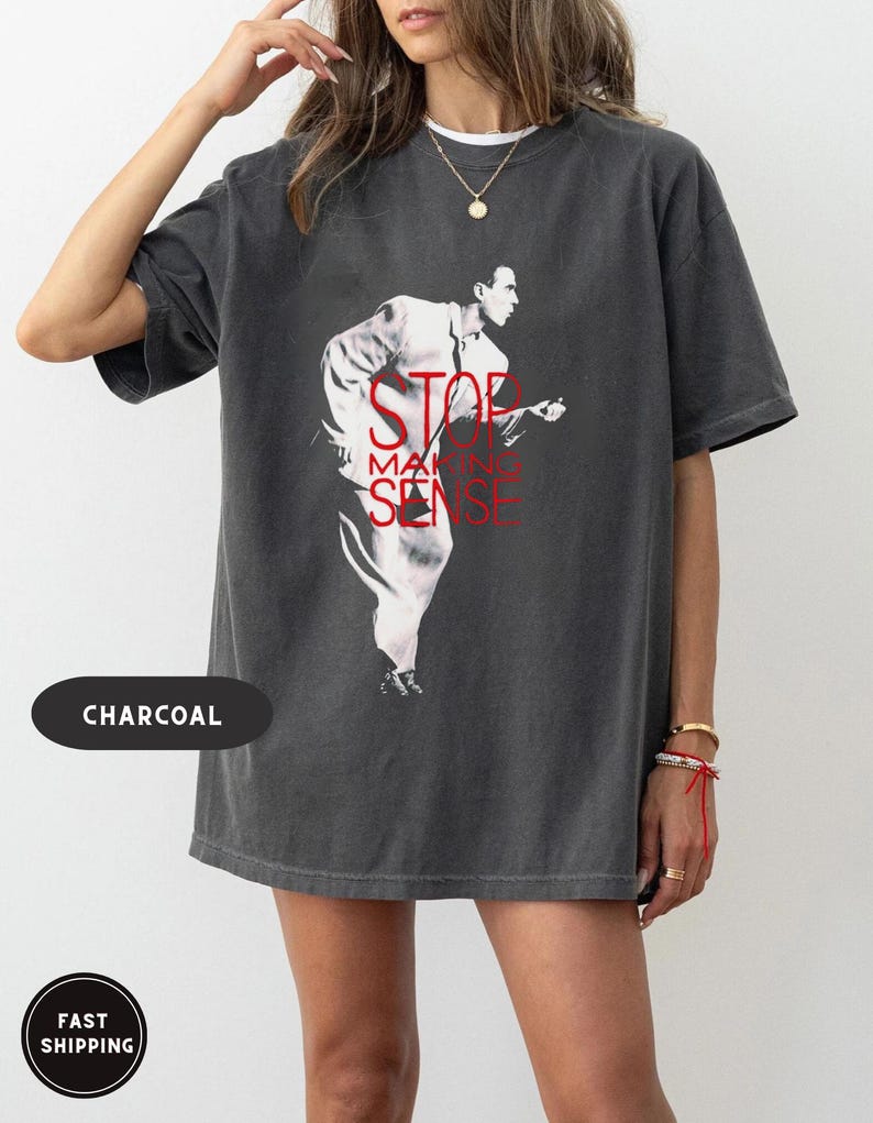 May include: Charcoal-colored t-shirt featuring a graphic of a man in a white suit with the text "STOP MAKING SENSE" in red. The shirt has a vintage, washed look.