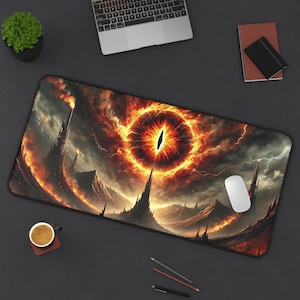 May include: A rectangular desk mat featuring a fantasy landscape with a fiery eye design. The artwork depicts a dark, mountainous terrain with a glowing orange and red eye in the center, surrounded by lightning and dark clouds. A white computer mouse is visible.