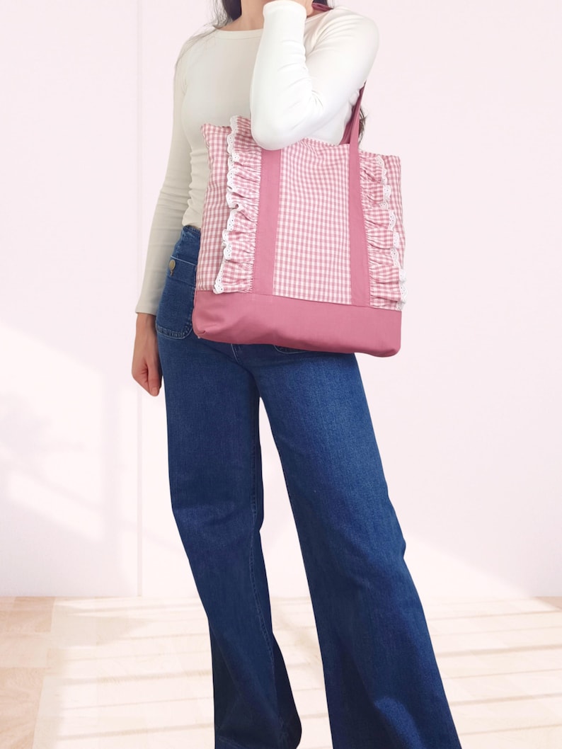 May include: A pink and white gingham tote bag featuring vertical pink fabric straps, ruffled side panels with white lace trim, and a solid pink base. The bag has two shoulder straps and is constructed from a combination of patterned and solid fabric.