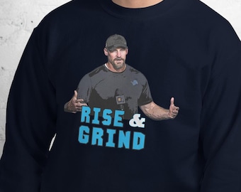 May include: A navy blue sweatshirt with a graphic of a man wearing a baseball cap and a black shirt. The graphic says "Rise & Grind" in blue text.