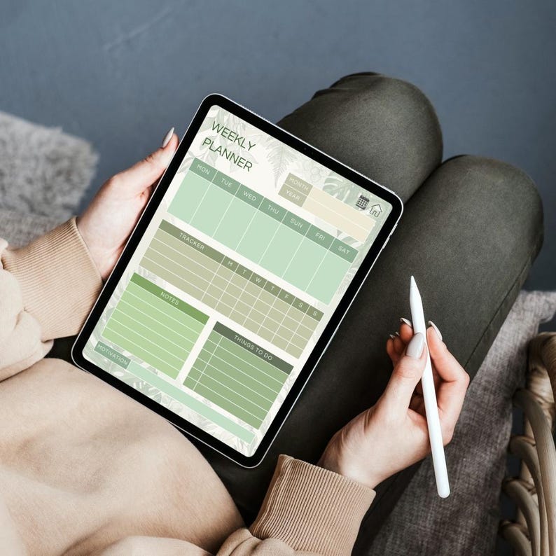 May include: A digital tablet displaying a weekly planner layout in shades of green. The screen shows sections for each day, a tracker, notes, and to-do lists. A white stylus is held nearby. The tablet is held on a person's lap.
