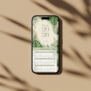 May include: A smartphone displays a digital planner for the year 2026. The screen features a calendar layout with a botanical design, including green leaves and the text "Planner 2026". The phone is set against a neutral background.