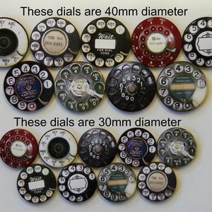 May include: A collection of 14 vintage rotary phone dials, some with black and white designs, others with red and white designs. The dials are 40mm and 30mm in diameter. Some dials have the words "Wait for dial tone" printed on them.