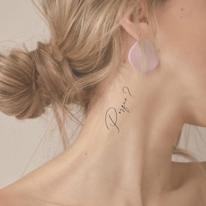 Może przedstawiać: Zbliżenie na szyję osoby z małym tatuażem, na którym widnieje napis "Porque?" w ozdobnym piśmie.