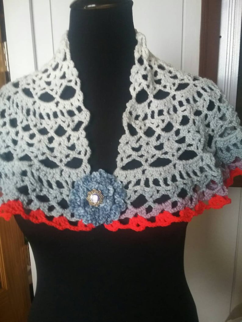 Shawl trimmed in red two fasteners pins one red one blue crocheted by hand.