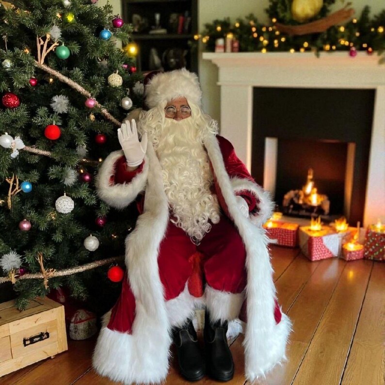 May include: Santa Claus in a red velvet suit with white fur trim, waving. He wears a white beard, hat, and gloves. A decorated Christmas tree and fireplace with candles are in the background.