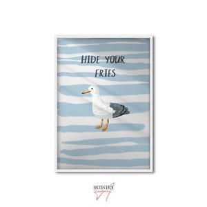 May include: A framed art print featuring a watercolor illustration of a seagull. The seagull is white with gray wings and yellow feet, set against a blue and white striped background. The text "HIDE YOUR FRIES" is at the top.