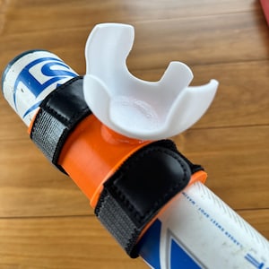 May include: A white plastic cup holder attached to a baseball bat with a black strap. The bat is orange and white with the text "LANCER SWEET SPOT - MATTE" printed on it.