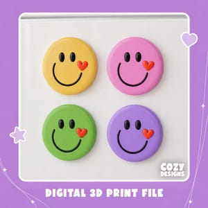 May include: Four circular magnets featuring smiley faces in yellow, pink, green, and purple. Each face has black oval eyes, a black curved mouth, and a small red heart accent near the mouth. The text COZY DESIGNS DIGITAL 3D PRINT FILE is visible.