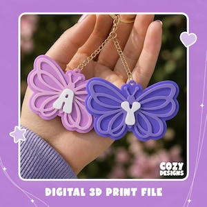 May include: Two butterfly-shaped keychains in light purple and dark purple, each featuring a white letter A or Y in the center. The keychains are attached to gold-colored metal chains and rings. The text COZY DESIGNS and DIGITAL 3D PRINT FILE is visible.