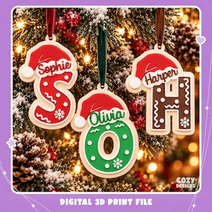 Op de afbeelding: Drie gepersonaliseerde kerstornamenten in de vorm van de letters S, O en H, elk bekroond met een rode kerstmuts. De letters zijn rood, groen en bruin met witte sneeuwvlok- en golfdetails. Elk ornament is voorzien van een naam: Sophie, Olivia of Harper.